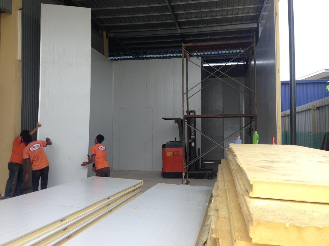 Workers in orange shirts fitting white insulated cold room panels